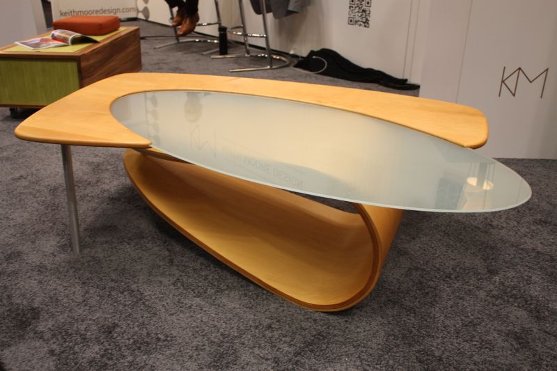 The "Fling" coffee table by Keith Moore Designs is modern and futuristic with a soft edge. The curvy wood and oval frosted glass keep the piece from being too cold.