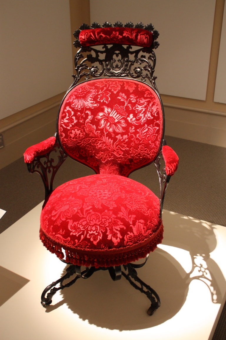 The armchair is fashioned from cast iron, wood, sheet metal, velvet, and faux rosewood graining.